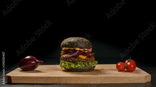 An appetizing black hamburger on a wooden board with fresh vegetables. photo