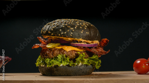 An appetizing black hamburger on a wooden board with fresh vegetables. photo