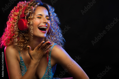 Attractive dancing woman with curly hair and red headphones in black background, neon light, motion effects. Copyspace.