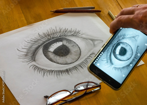 The hand of the artist is making the photo from of the woman's eye made by himself in grayscale. The picture is on the white paper. The picture of this composition made by middleformat camera. photo