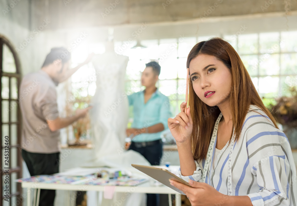Fototapeta premium Young asian confident fashion designer-clothes women and team are thinking and working for work fashion design at studio. Happy work for successful . Teamwork fashion designer concept