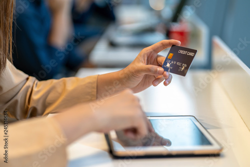 Closeup Asian woman using credit card with tablet for online shopping in department store over the clothes shop store background, technology money wallet and online payment concept, credit card mockup
