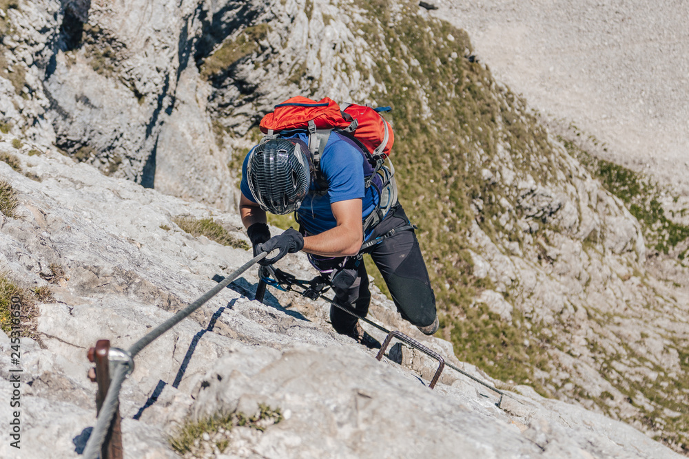 A climber climbing via ferrata. Adventure extreme ascent of an alpine rock wall. Summer mountain sport adventure. Man climbing ferrata. A climber climbing via ferrata. Adventure extreme ascent of an alpine rock wall. Summer mountain sport adventure. Man climbing ferrata.