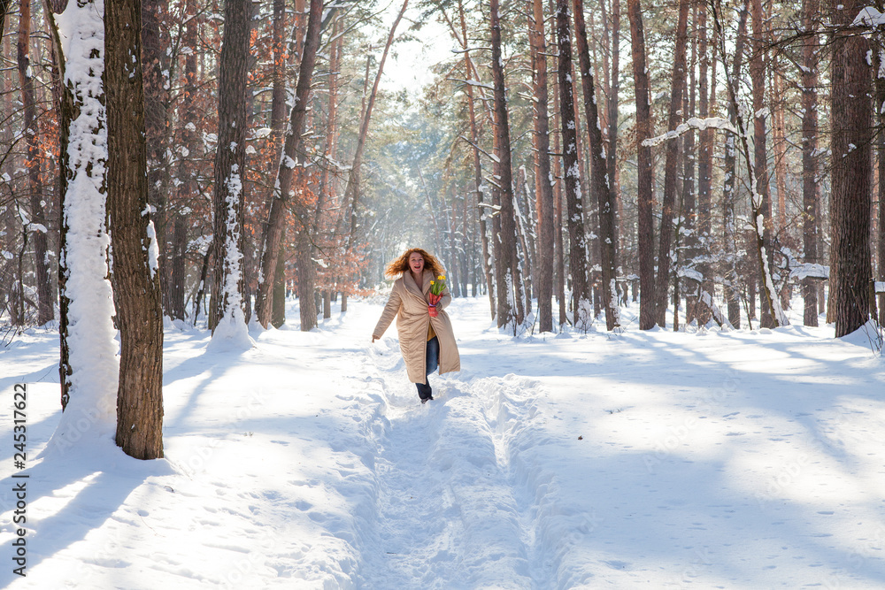 Full length of delighted red haired woman running through winter forest with narcissus in hand