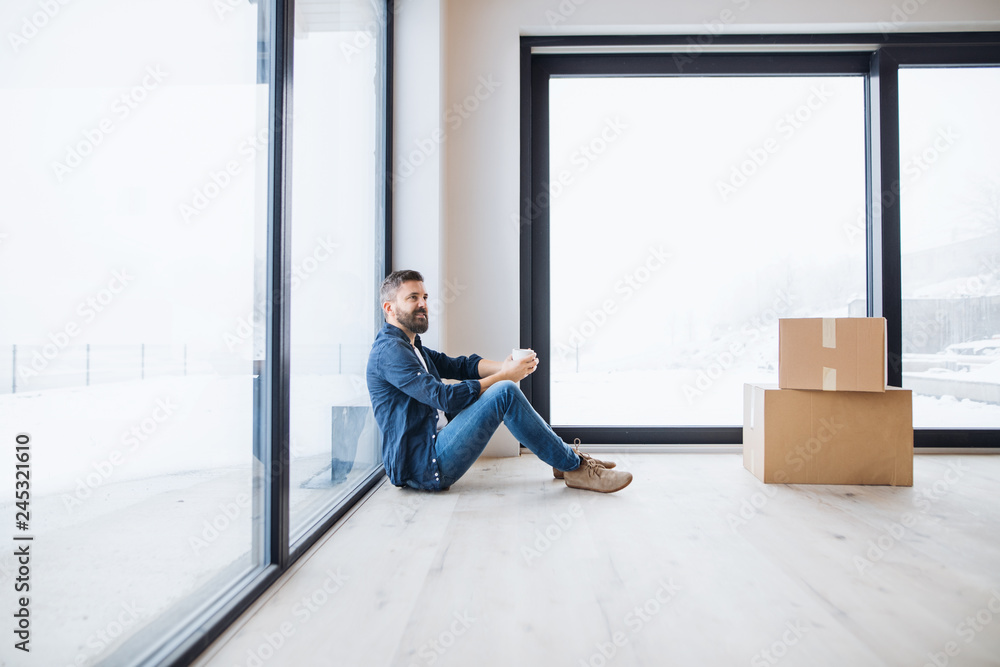 A mature man with cardboard boxes sitting on the floor, furnishing new house.