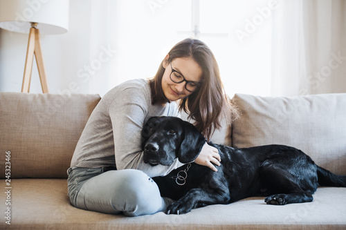 Teenage girl sitting on a sofa indoors, playing with a pet dog. photo