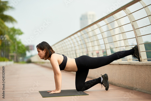 Side view of Asian woman training on waterfront stretching body in daylight
