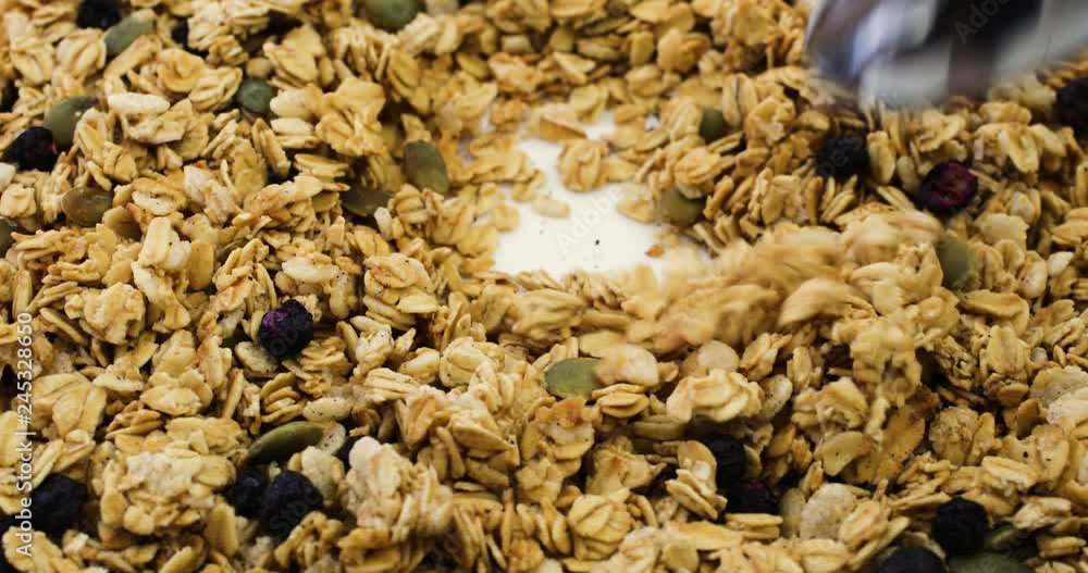 Close video of stirring dry organic breakfast cereal with dried blueberries and pumpkin seeds on a white plate then taking a spoonful at the end. Close video of stirring dry organic breakfast cereal with dried blueberries and pumpkin seeds on a white plate then taking a spoonful at the end.