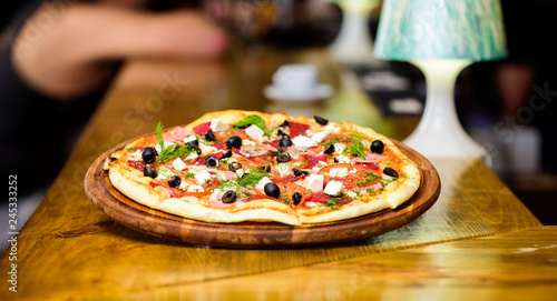 Pizzeria restaurant. Italian pizza concept. Delicious hot pizza on wooden board plate. Food delivery service. Pizza served with dill. Pizza with tomatoes black olives and ham. Take away food concept