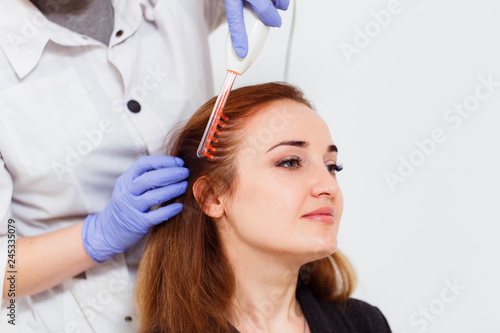 A young woman visited a dermatologist. Receiving electric darsonval facial massage procedure at beauty salon. White background