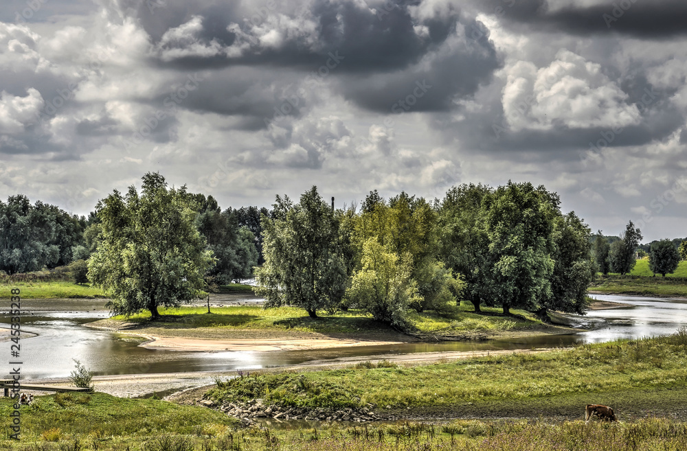 Small island with trees, bushes and sandy beaches in a secondary channel of the river Waal, near Tiel, The Netherlands, under a dramatic sky Small island with trees, bushes and sandy beaches in a secondary channel of the river Waal, near Tiel, The Netherlands, under a dramatic sky
