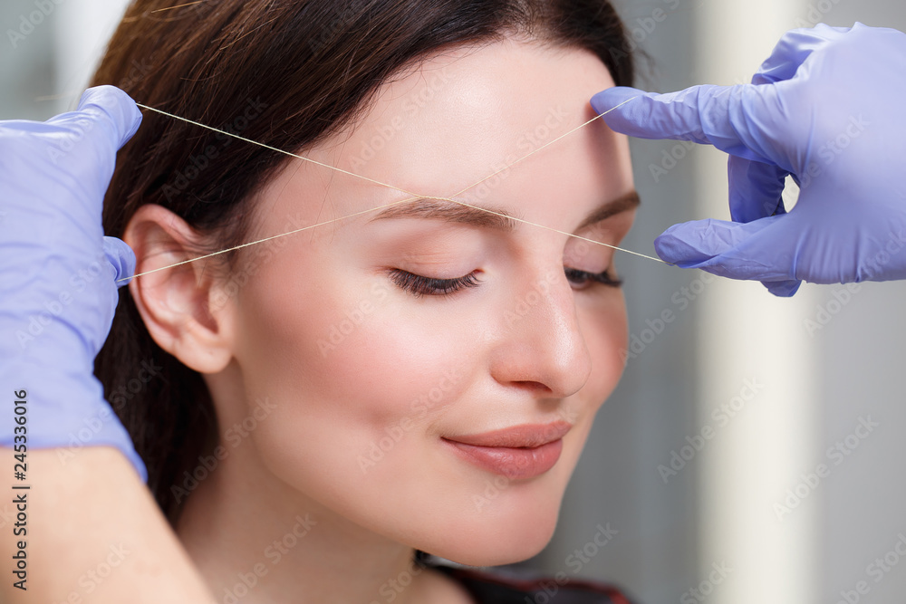 Cosmetologist plucks client eyebrows by thread. Close up Cosmetologist plucks client eyebrows by thread. Close up