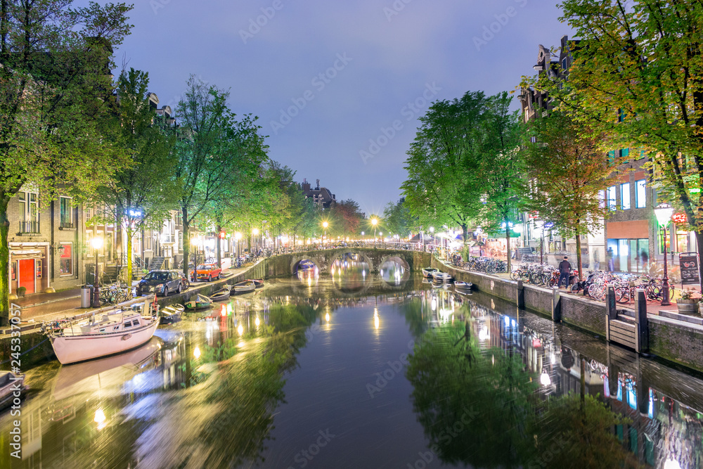Canal with boats and bicycles on the street at night in Amsterdam, Holland