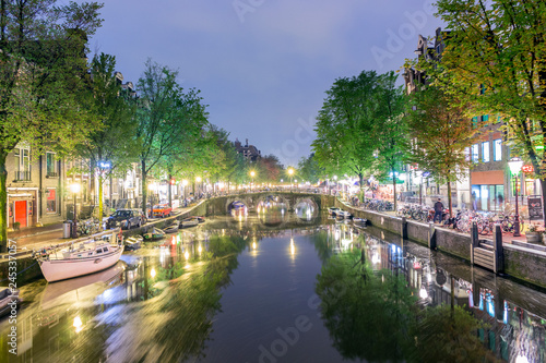 Canal with boats and bicycles on the street at night in Amsterdam, Holland