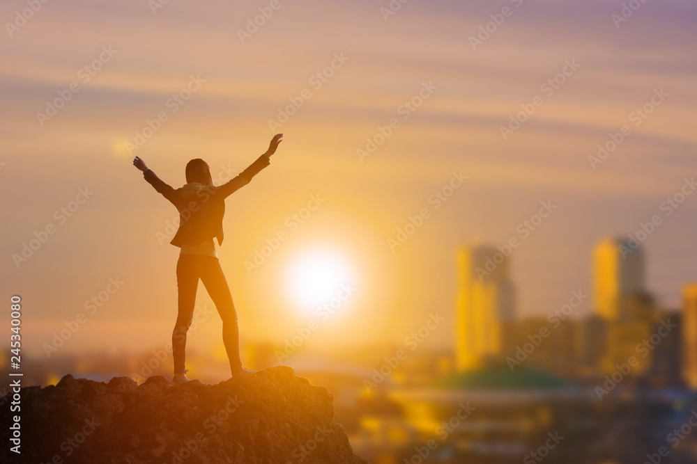 Slender girl businessman on top of a mountain holding her hand up, against the background of the city in the rays of the sun. Business concept idea, happiness, success and achievement, leadership. Slender girl businessman on top of a mountain holding her hand up, against the background of the city in the rays of the sun. Business concept idea, happiness, success and achievement, leadership.