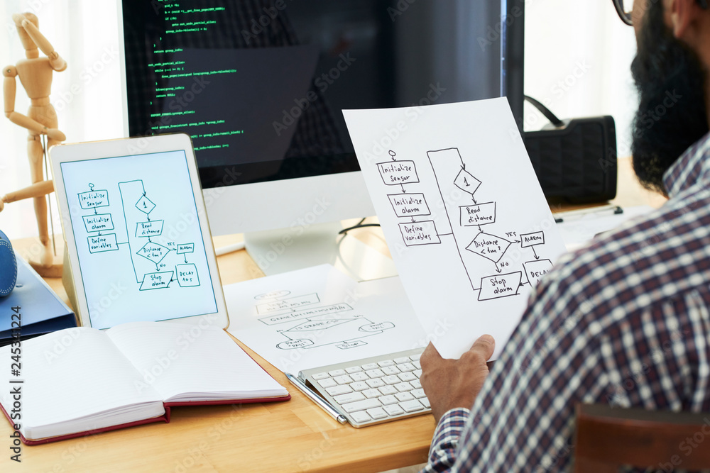 Obraz premium Contemporary it developer looking through papers with sketches of schemes while learning data decoding points