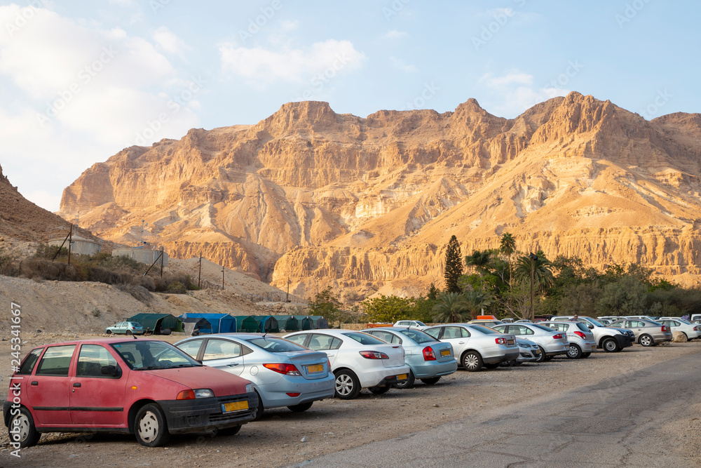 Car park at Ein Gedi - National park and resort view of  Negev desert mountain landscape in Israel. A small group of hikers walking on the path.