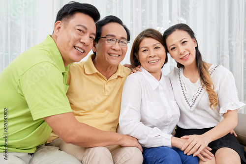 Group of ethnic adult and mature people sitting together on sofa at home smiling at camera
