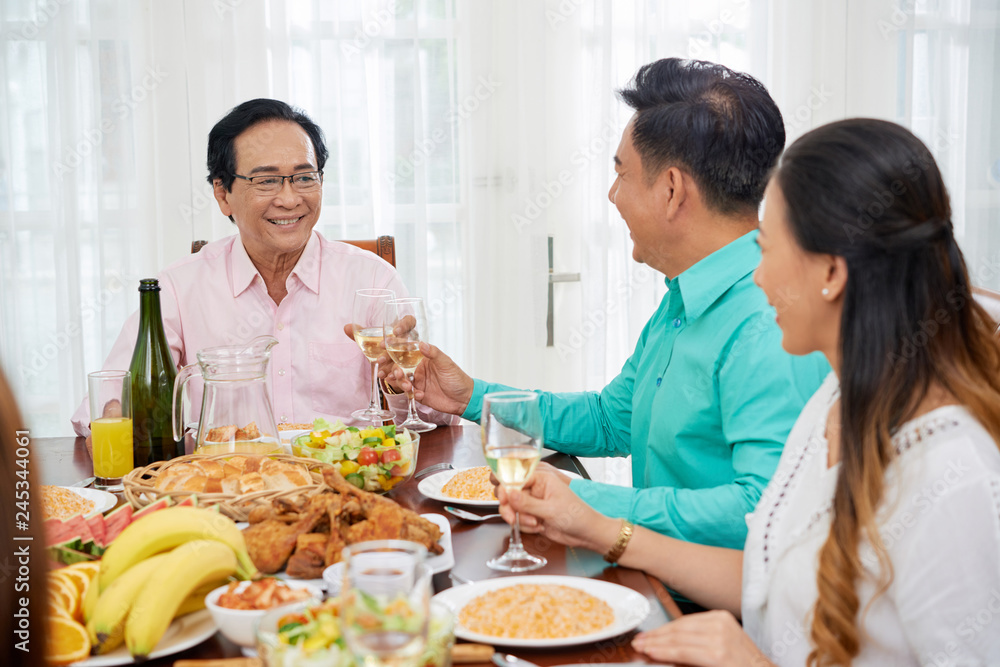 Asian family having delicious meal and clinking with glasses at table on dinner spending time together