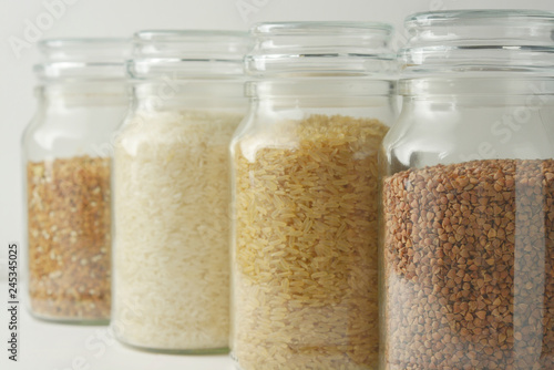 Various raw cereals, grains, rise, buckwheat and flakes. Healthy cooking in glass jars, white background. Clean eating, vegetarian, vegan, balanced dieting food concept