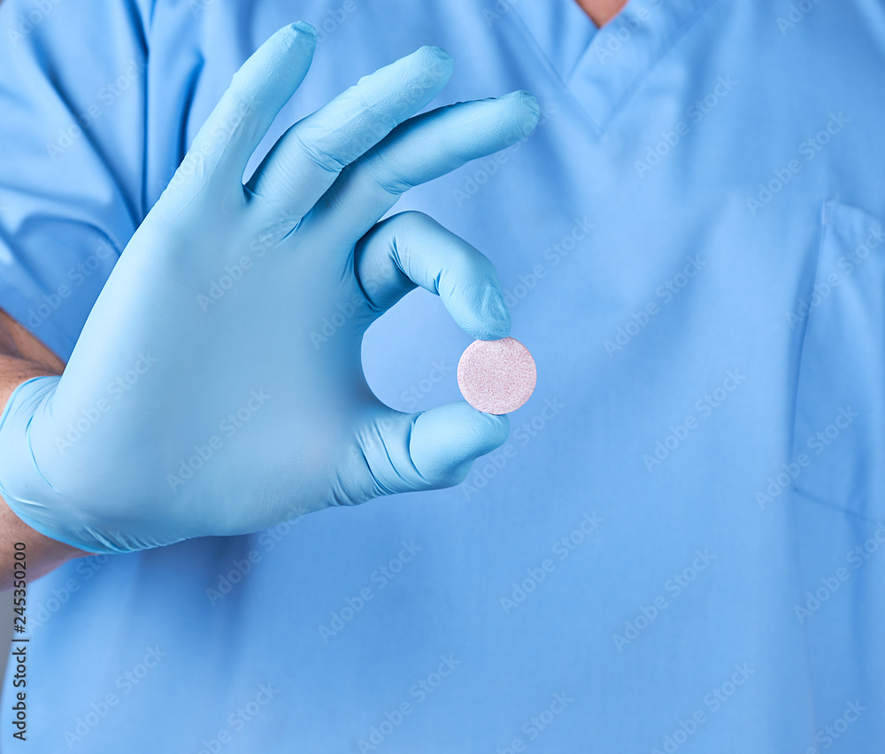 Fototapeta premium doctor in blue latex gloves holding a large round pill