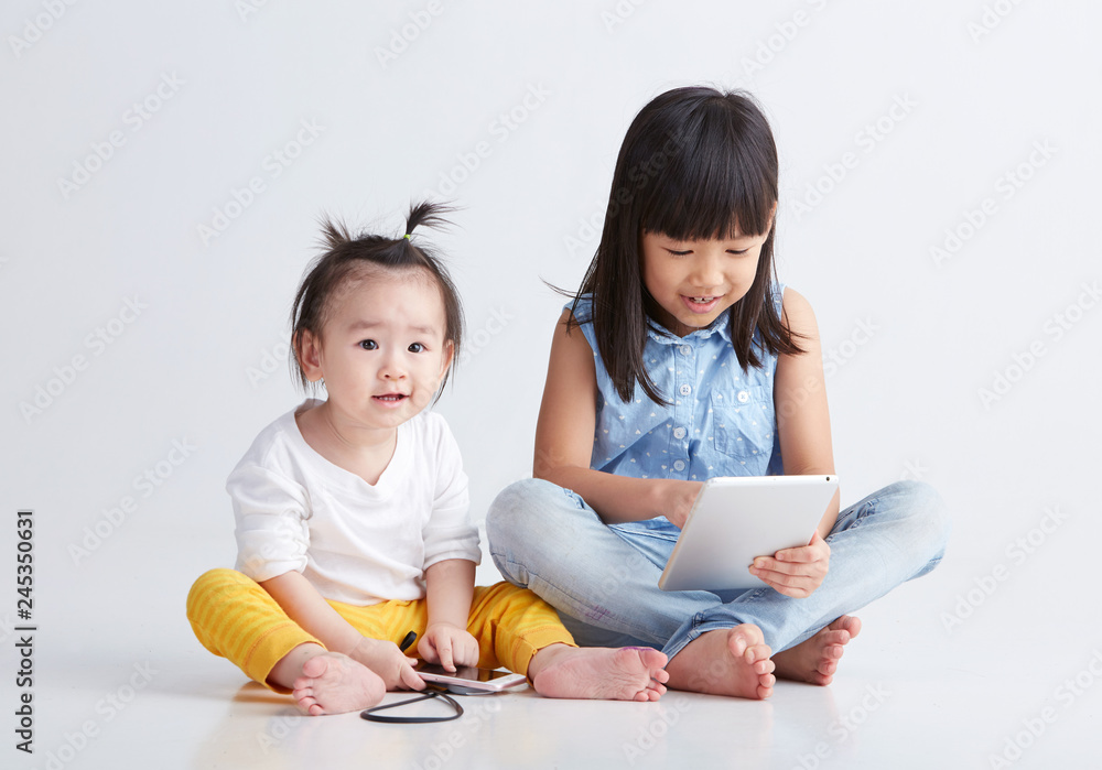 Asian little sisters are playing with digital product, on white background Asian little sisters are playing with digital product, on white background