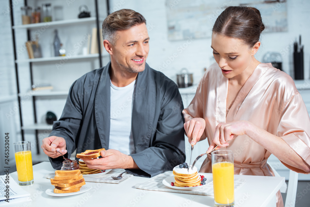 beautiful adult couple in robes during breakfast with pancakes and orange juice in kitchen