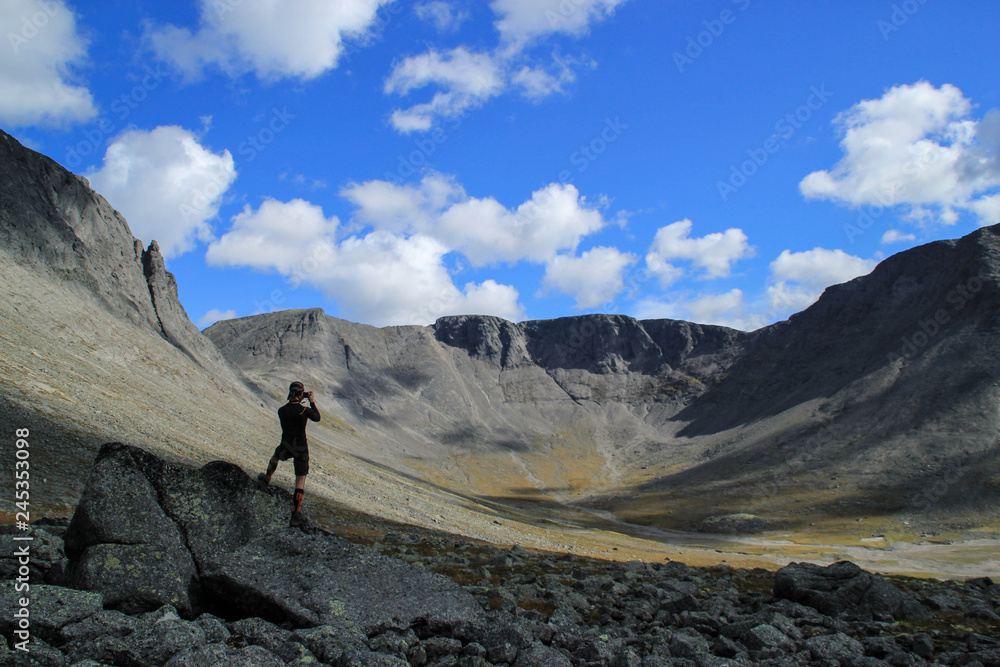 Young white Caucasian male tourist takes photo of beautiful mountains on a sunny summer day