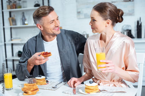 husband and wife in robes during breakfast with pancakes and orange juice in kitchen
