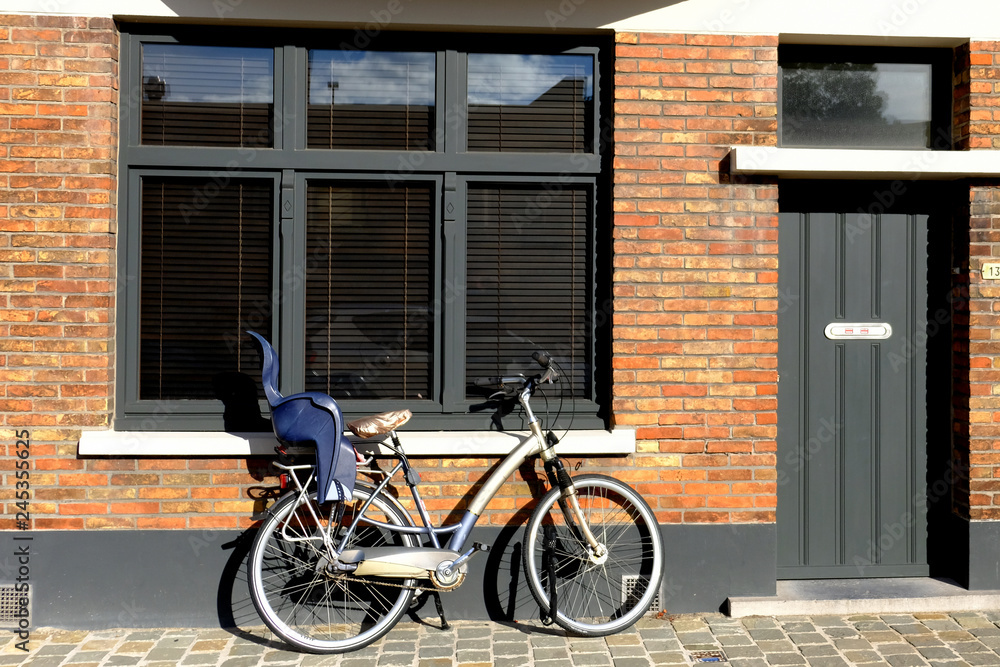 bike with a child seat near the wall of a brick house, next to the window and the door
