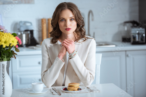 beautiful woman sitting at table with pancakes and coffee during breakfast in kitchen