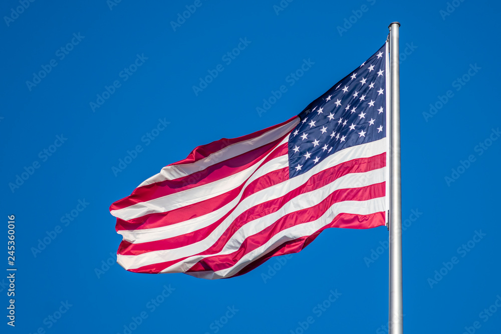 Flag of United States of America waving in wind, against clear sky Flag of United States of America waving in wind, against clear sky