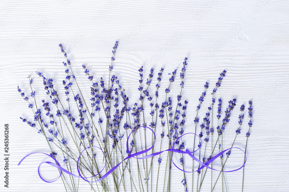 Obraz premium Lavender flowers and ribbon on white wooden background withcopy space. Branches of lavender on wood.