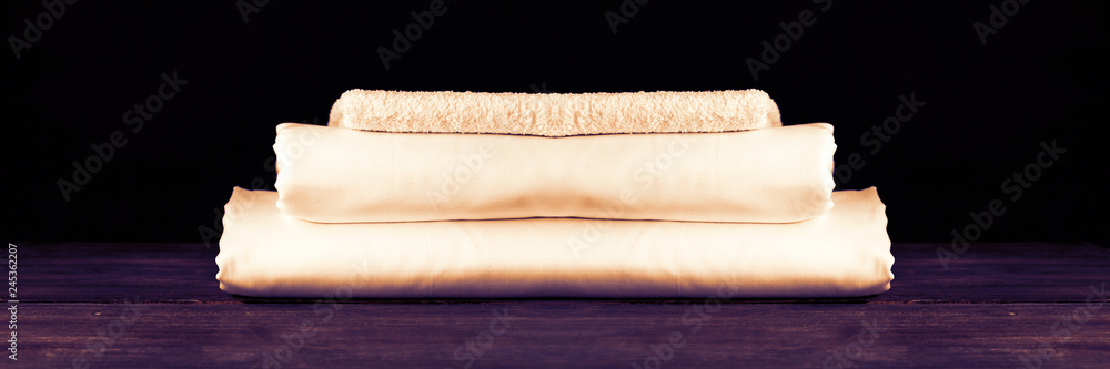 Stack of white clean new bed sheets on wooden desk against black background. Copy space. Concept of comfortable and stylish rest and dream.. Wide panoramic image.