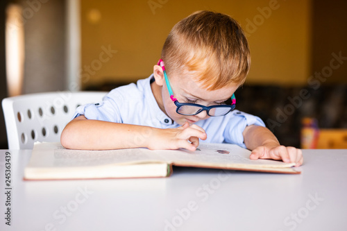 Cute toddler boy with down syndrome with big glasses reading intesting book photo