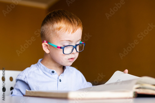 Cute toddler boy with down syndrome with big glasses reading intesting book photo