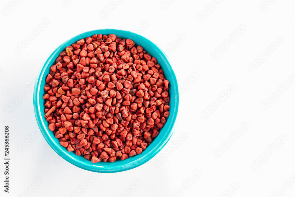 annatto seeds in blue bowl, isolated on white background annatto seeds in blue bowl, isolated on white background