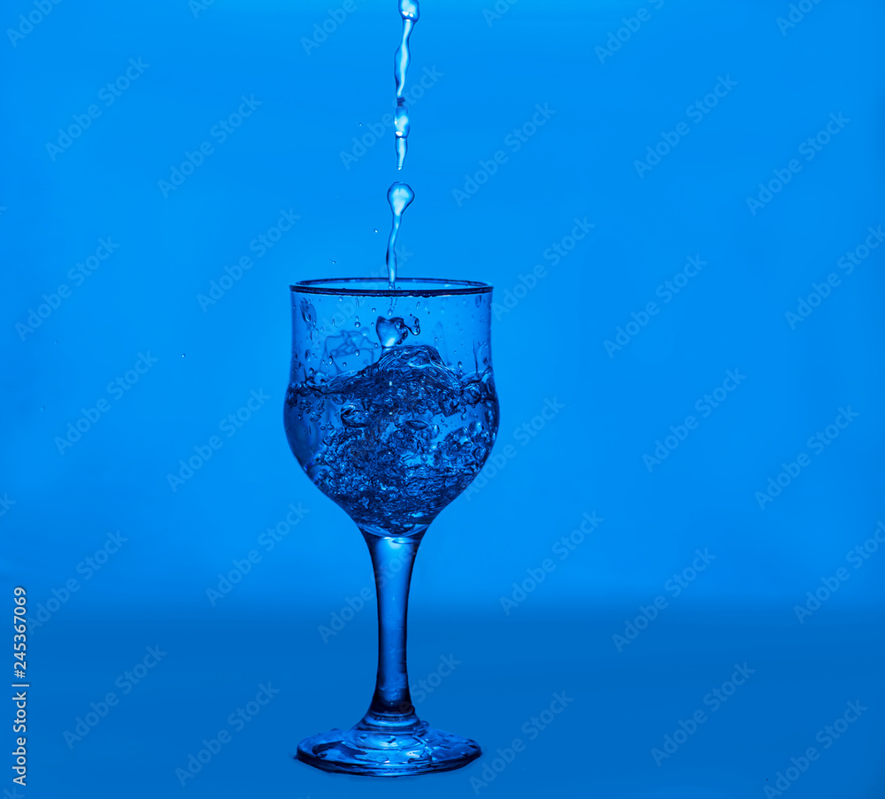 Splashes of water. Glass on a blue background. Minimal night party life concept Splashes of water. Glass on a blue background. Minimal night party life concept