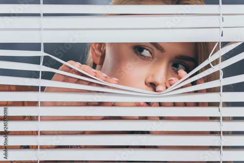 Bilde på lerret young woman looking away and peeking through blinds, mistrust concept