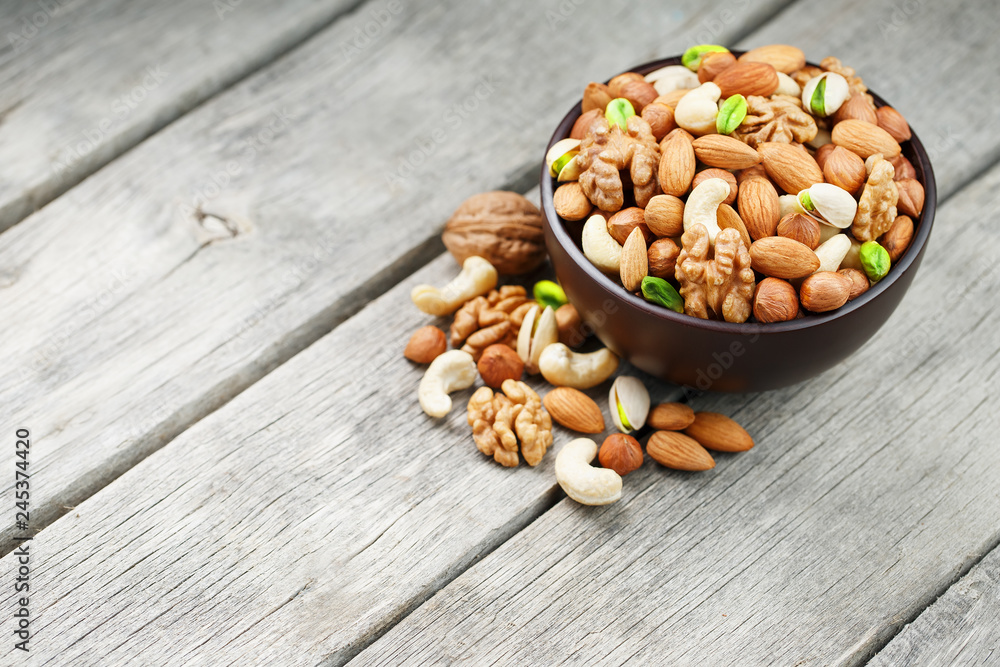 Wooden bowl with mixed nuts on a wooden gray background. Walnut, pistachios, almonds, hazelnuts and cashews, walnut. Wooden bowl with mixed nuts on a wooden gray background. Walnut, pistachios, almonds, hazelnuts and cashews, walnut.