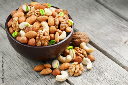 Wooden bowl with mixed nuts on a wooden gray background. Walnut, pistachios, almonds, hazelnuts and cashews, walnut.
