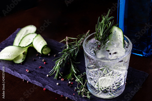Gin-tonic alcoholic cocktail. Cucumber, rosemary, ice. On a black wooden background.