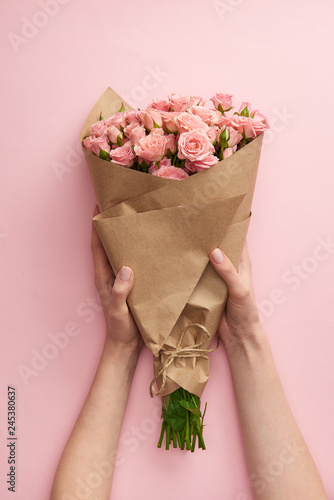 Fotografie cropped shot of female hands holding bouquet of beautiful pink roses wrapped in