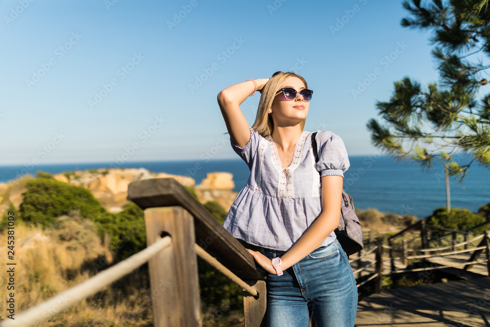 Young woman in sunglasses posing on the promenade of the stone beach with sea on background