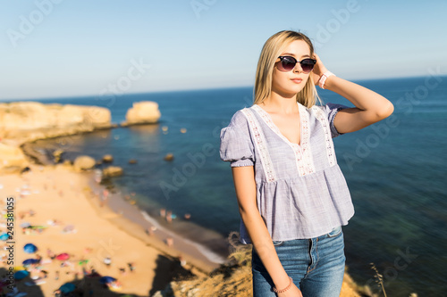 Young pretty woman standing on the edge of the rock coast with beautiful view on the sea coast