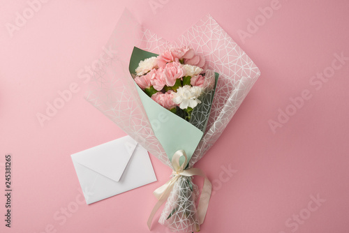 top view of beautiful tender flower bouquet and white envelope isolated on pink