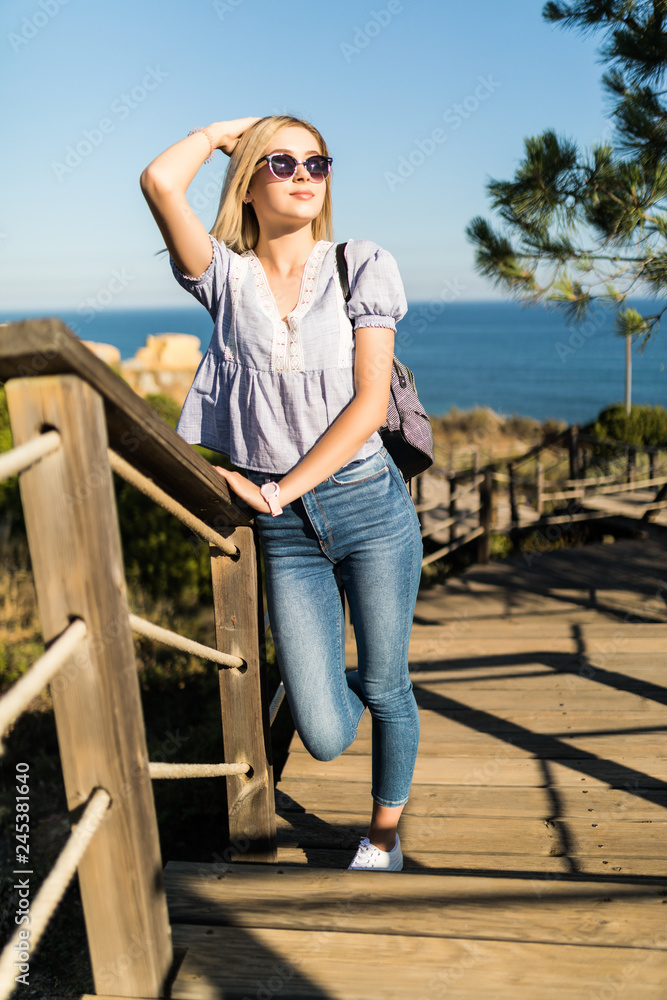 Young blonde woman in sunglasses with bag walking on the stair on the way to the sea beach