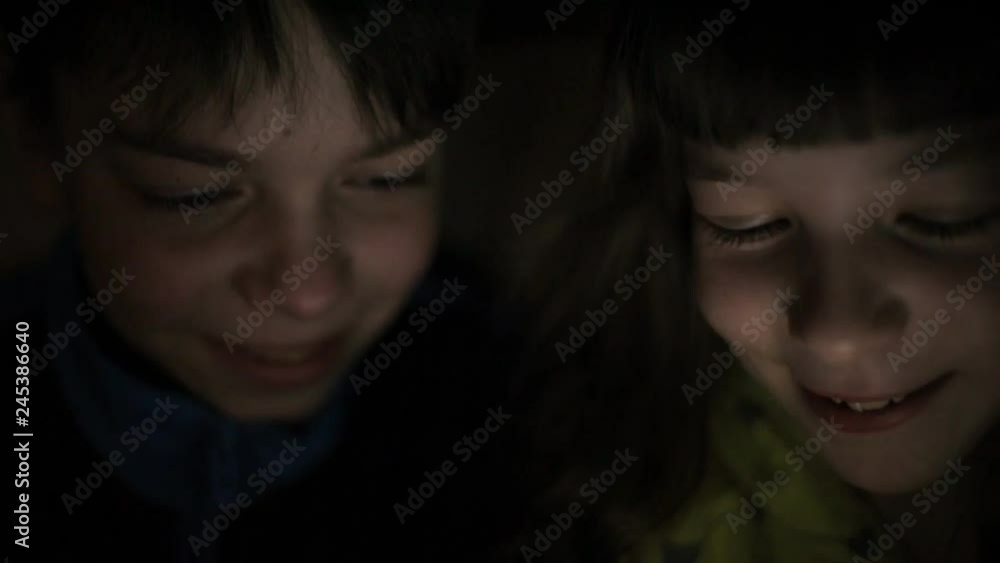 Night the faces of the children , brother and sister browsing a tablet PC with the reflection of light on them Night the faces of the children , brother and sister browsing a tablet PC with the reflection of light on them