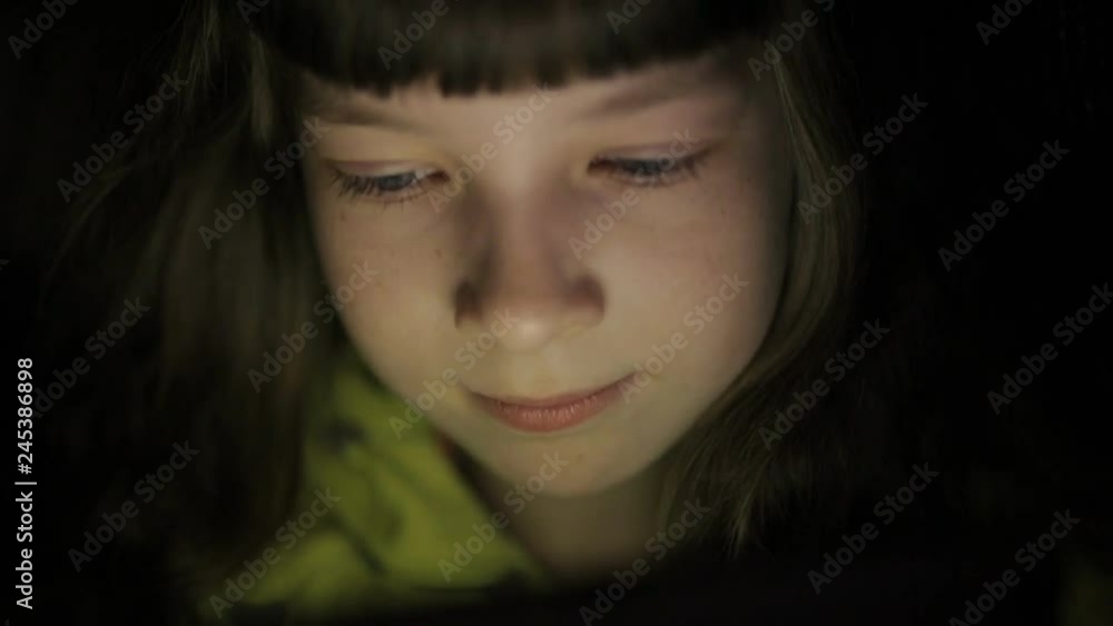 Night shot of kid's girl face browsing tablet pc with light reflection on it Night shot of kid's girl face browsing tablet pc with light reflection on it