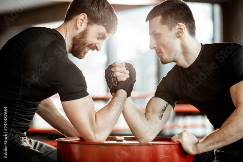 Quadro su tela Two young athletes in black sportswear having a hard arm wrestling competition o